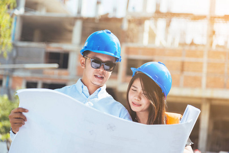亞洲男女工程師與藍色安全頭盔會議在建筑工地與藍圖照片